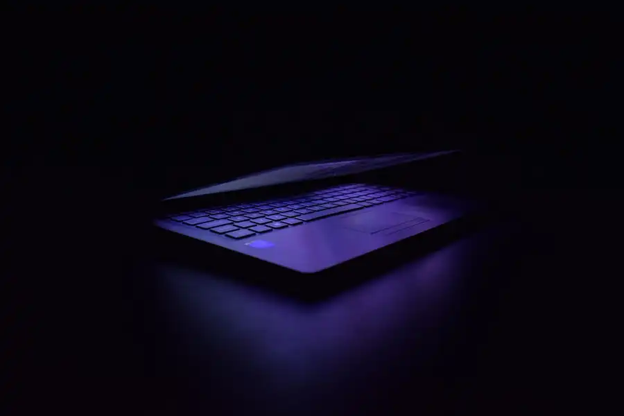 Notebook aberto numa sala escura, com luz violeta